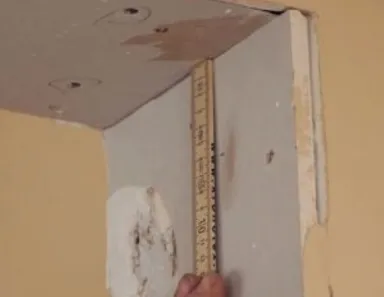 Person, die mit einem Lineal die Abmessungen einer Trockenbauwand an einem unfertigen Türrahmen und einer Wandecke misst.