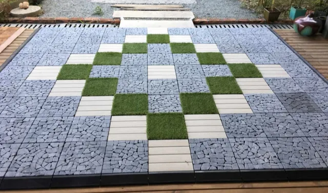 Quadratische Terrasse mit grauen Klickfliesen, grünen Grasflecken und Holz in einem Muster.