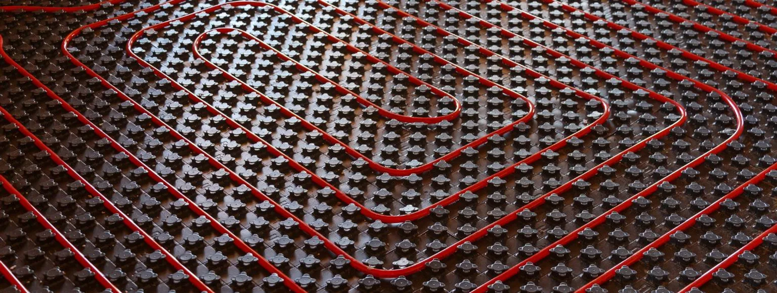 Rote Fußbodenheizungsrohre, die bei der Verlegung spiralförmig auf einer dunklen Matte verlegt werden.