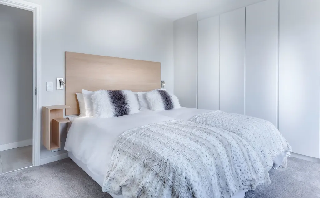 Schlafzimmer mit weißen Möbeln, flauschigen Kissen und neutralen Farben, minimalistisch gestaltet.