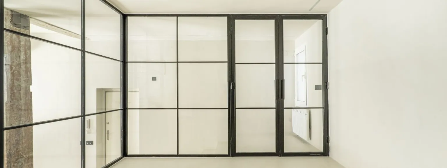 Schwarz gerahmte Lofttüren und Glasscheiben trennen einen lichtdurchfluteten, minimalistischen Innenraum.