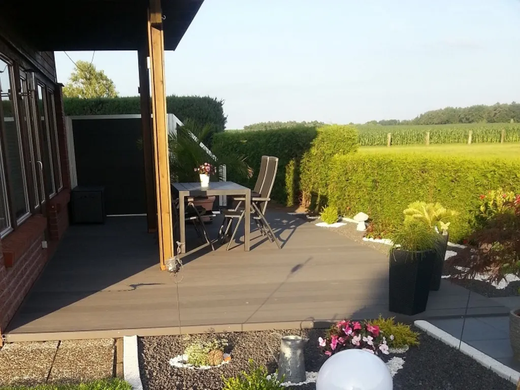 Terrasse mit Tisch und Stühlen auf einer sauberen WPC-Terrasse, mit Blick auf den grünen Gartenbereich.