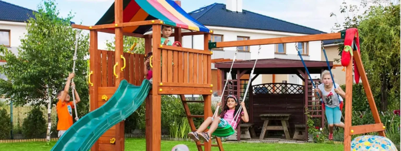 Vier Kinder klettern auf einem bunten Spielturm in einem Außenbereich.