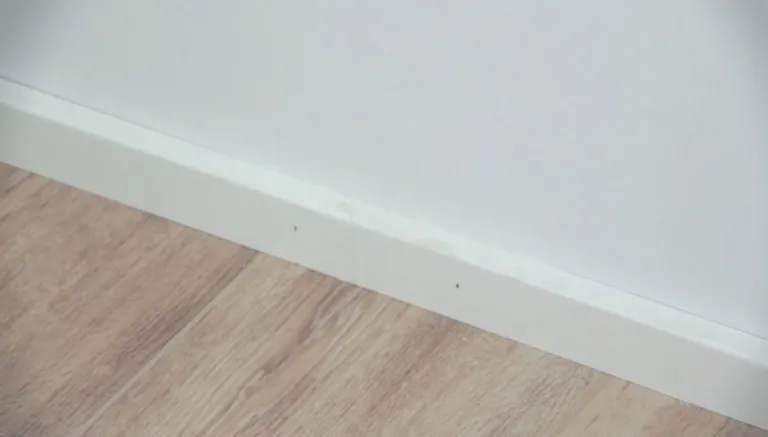 Weiße Sockelleiste mit einer kleinen Delle über hellem Laminatboden und einer weißen Wand.