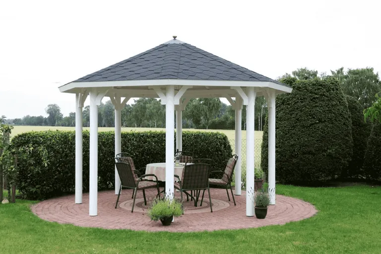 Weißer Gartenpavillon mit Tisch und Stühlen auf einer roten Backsteinterrasse, umgeben von grünem Rasen.