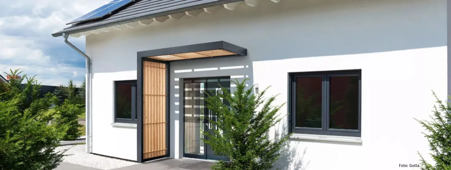Weißes, modernes Haus mit dunklen Fensterrahmen und einem passenden hölzernen Vordach an der Vorderseite.