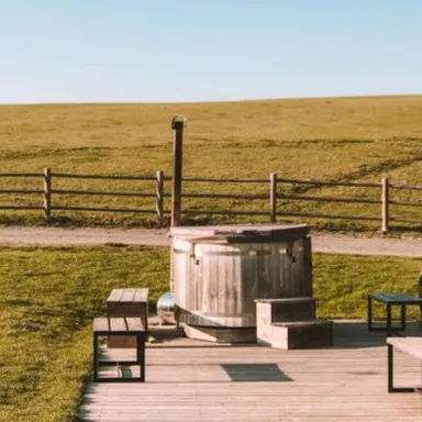Whirlpool aus Holz auf einer Terrasse mit Blick auf eine grüne Wiese im Hintergrund.