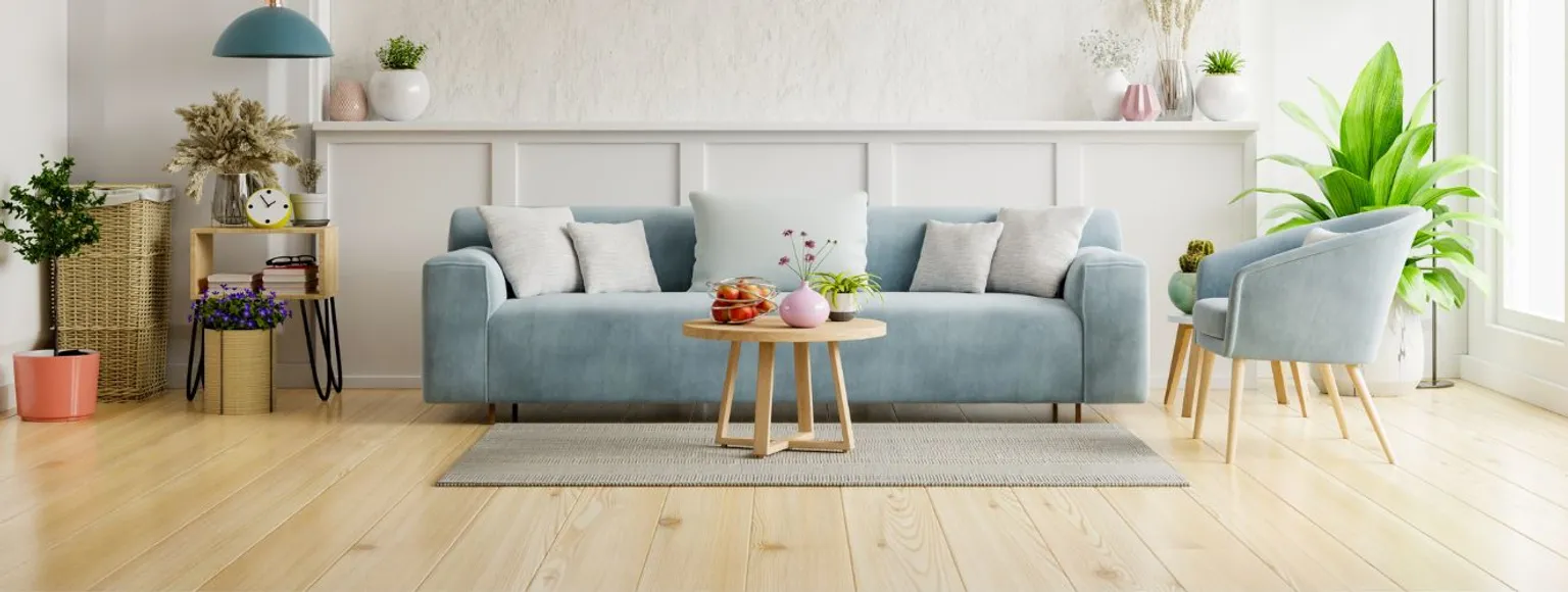 Wohnzimmer mit blauem Sofa, Holzfußboden, Grünpflanzen und einem Couchtisch aus Holz.