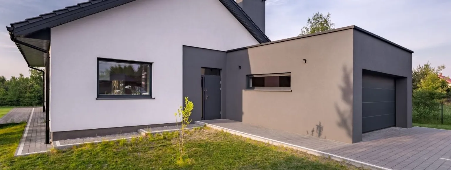Zeitgenössisches Haus mit grau-weißer Fassade, sichtbarer Garage und flach gepflasterter Auffahrt.