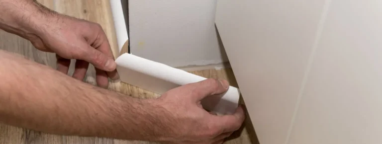 Hände montieren weiße Sockelleiste an hellem Holzfußboden