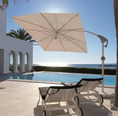 Zwei Liegestühle und ein weißer Sonnenschirm auf einer Terrasse am Meer im Licht des Sonnenuntergangs.