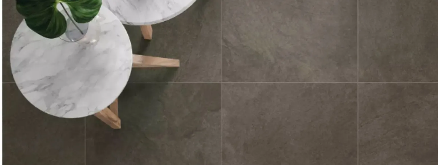 Zwei runde Marmortische stehen auf grauen DryTile-Bodenfliesen in einem neutralen Innenraum.