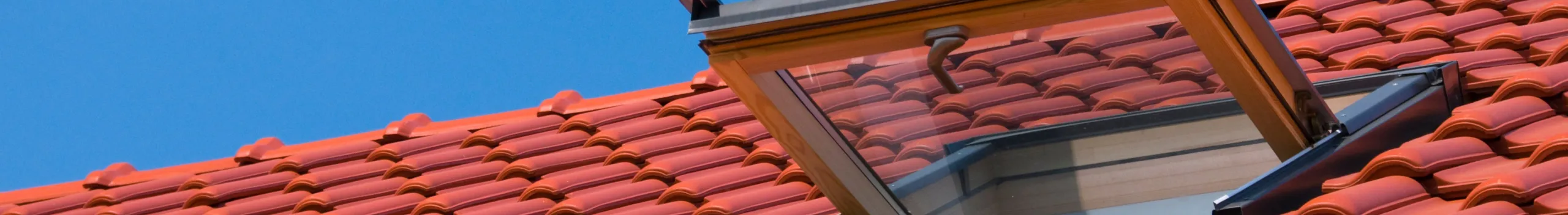 Ein offenes Fenster in einem roten Ziegeldach unter einem klaren blauen Himmel, Außenansicht gezeigt.