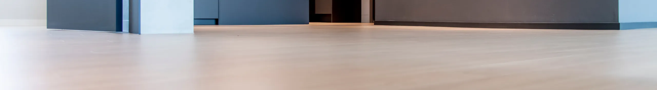 Heller Holzfußboden in einem modernen Raum mit dunklen Schränken und einem offenen Durchgang.