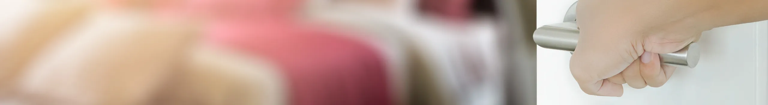 Person, die eine silberne Türklinke dreht, wobei im Hintergrund ein verschwommenes Schlafzimmer zu sehen ist.