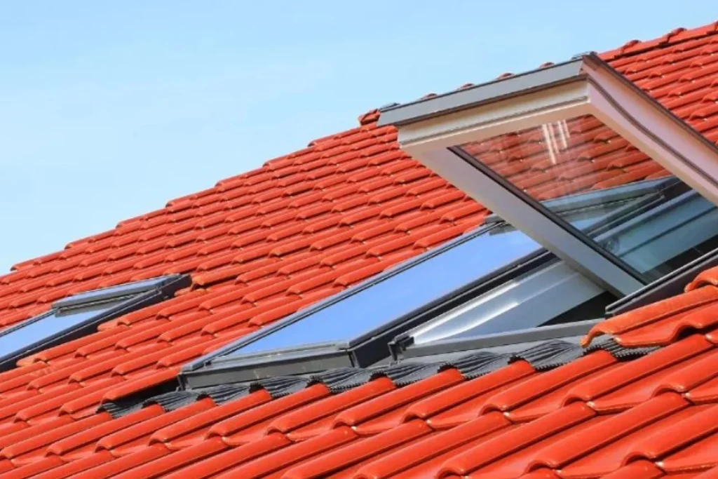 Rotes Ziegeldach mit einem offenen Fenster und einem Oberlicht vor einem klaren blauen Himmel.