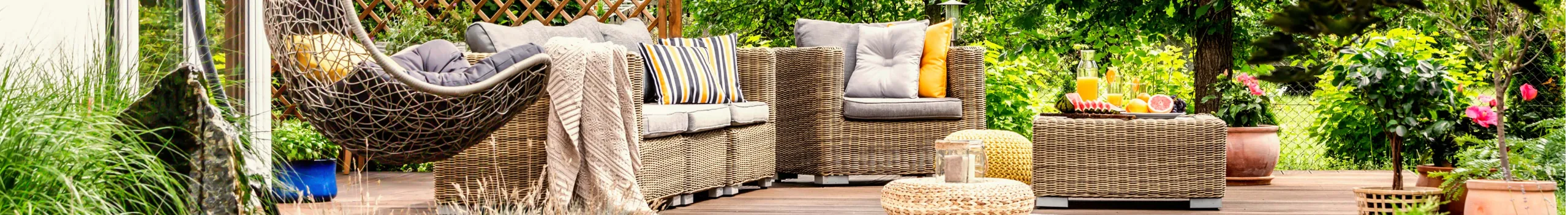 Terrassenmöbel aus Korbgeflecht und ein Hängesessel auf einem Balkon mit grüner Gartenumgebung.