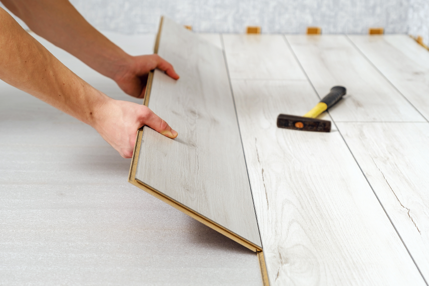 Zwei Hände verlegen hellen Holzlaminatboden mit Unterlage unter Vinylplatten auf dem Boden.