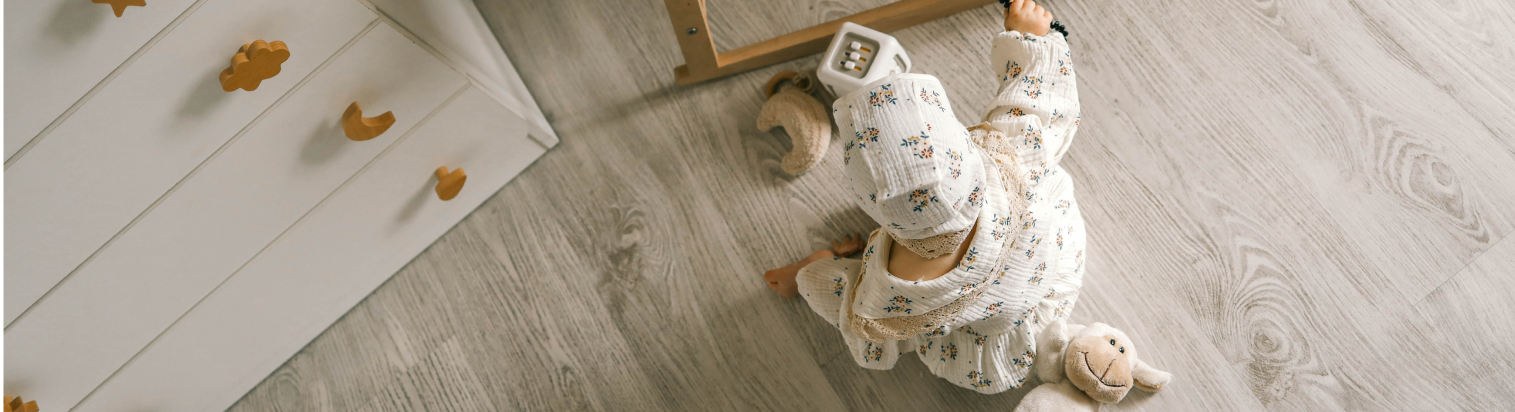 Ratgeber Titel Bild Baby sitzt auf hellem Vinylboden in Holzoptik und spielt mit Spielzeug