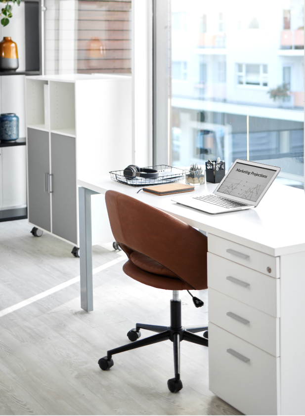 Bürotisch mit Laptop und Stuhl auf hellem Holzfußboden in der Nähe eines großen Fensters im Arbeitsbereich.