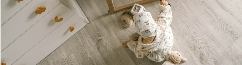 Ein Baby in einem geblümten Outfit sitzt auf dem Fußboden eines Kinderzimmers.