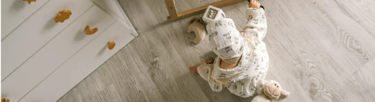 Ein Baby in einem geblümten Outfit sitzt auf dem Fußboden eines Kinderzimmers.