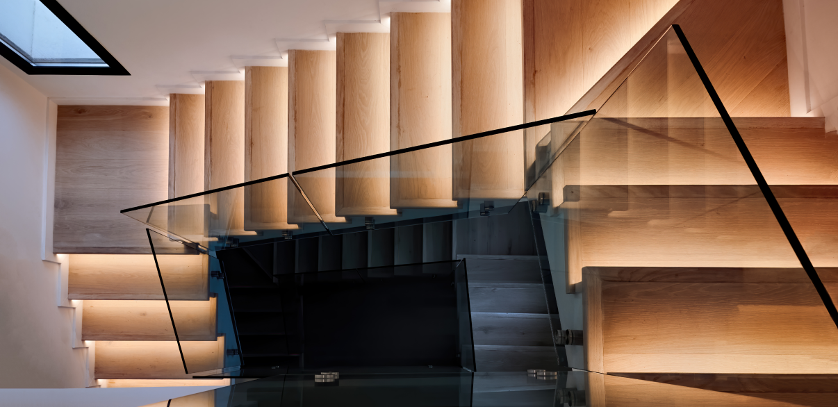 Moderne, offen gestaltete Treppe mit Vinyl-Trittstufen in Holzoptik, kombiniert mit seitlichem Glasgeländer und integrierter Stufenbeleuchtung – hochwertiges Beispiel für eine zeitgemäße Treppenrenovierung mit Vinylbelag