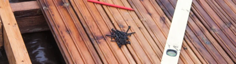 Schrauben Bleistift und Wasserwaage auf braunen Holzdielen für den Terrassenbau.