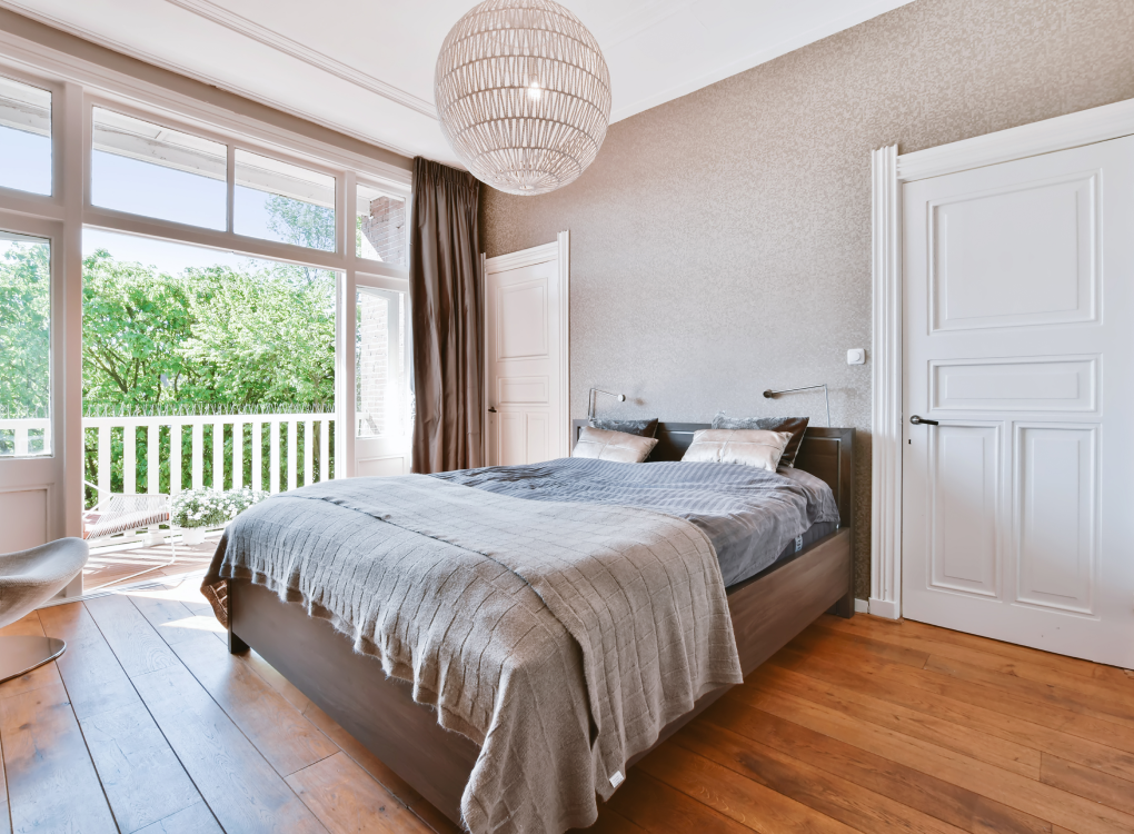 Freundlich eingerichtetes Schlafzimmer mit klassischem Eichenparkett, großen Fensterflächen und direktem Zugang zum Balkon – die warme Holzfarbe sorgt für Geborgenheit und natürlichen Charme. Das Bild ist klickbar und verlinkt zum passenden Produkt im casando-Shop.