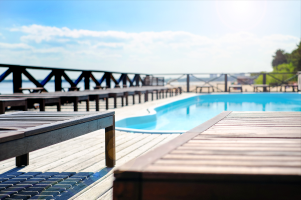 Moderne WPC-Terrassendielen rund um einen Pool im Sonnenlicht, mit stilvollen Liegen und Blick auf den Strand – klickbares Bild führt direkt zum passenden Produkt im casando Shop.