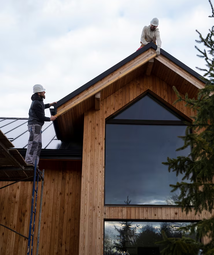 Zwei Arbeiter mit Helmen reparieren ein Ziegeldach während einer energieeffizienten Renovierung.