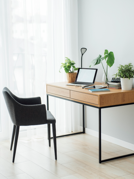 Heimbüro mit Holzboden, Schreibtisch, Laptop und Grünpflanzen in einem hellen Raum.