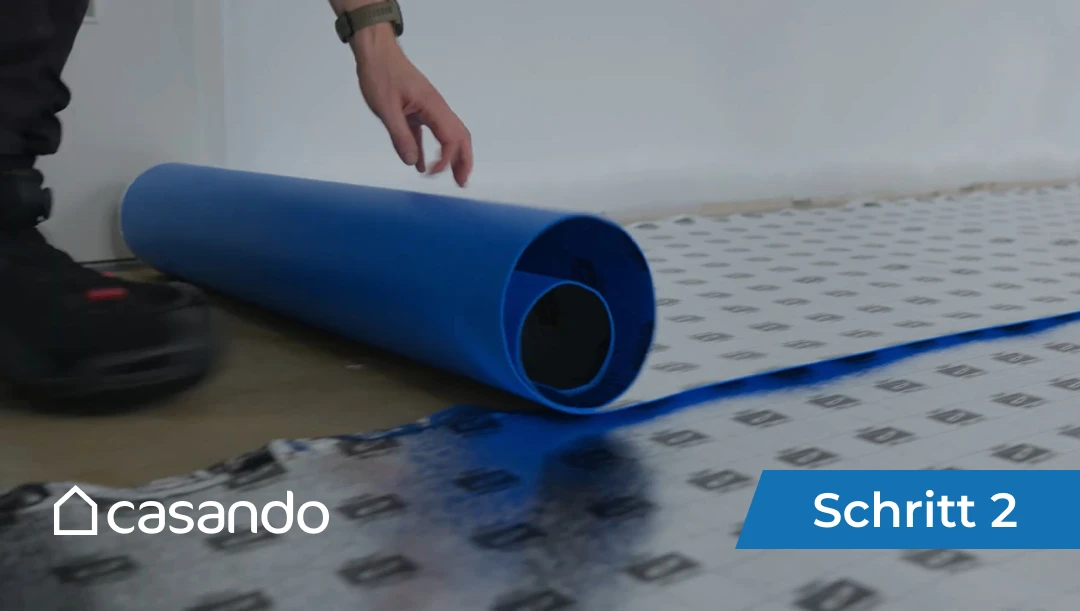Eine Person verlegt eine blaue Bodenunterlage auf dem Fußboden (siehe Videoübersicht unten).