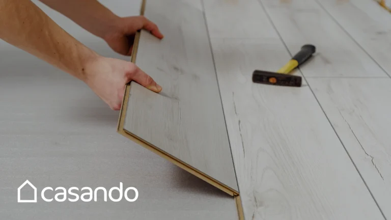 Person, die einen braunen Laminatfußboden mit Hammer und Zubehör verlegt, Casando-Logo sichtbar.