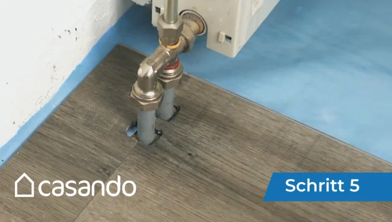 Screenshot aus einer Videoanleitung, die zeigt, wie Holzböden um Heizkörperrohre herum geschnitten werden, casando-Logo.