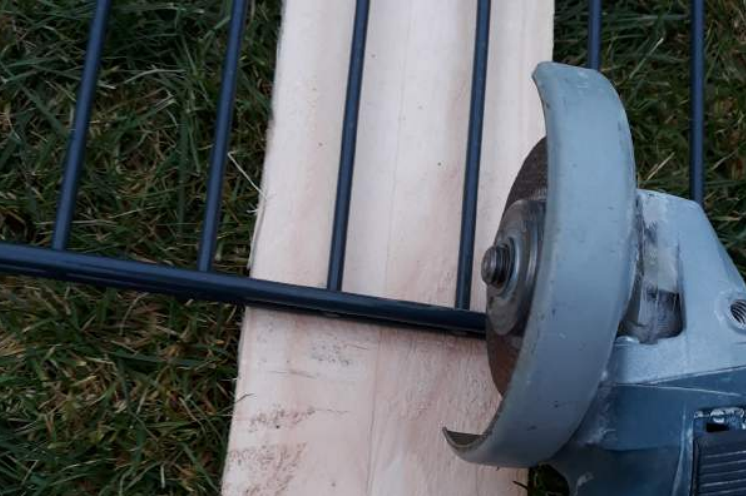 Eine Zaunmatte wird mithilfe einer Flex gekürzt.