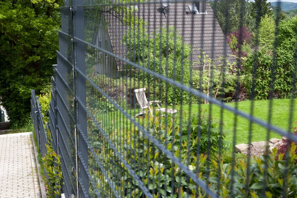 Ein Doppelstabmattenzaun steht versetzt auf einem Grundstück mit Gefälle.