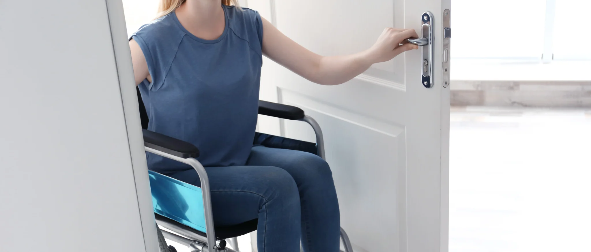 Eine Frau im Rollstuhl öffnet eine weiße Innentür.