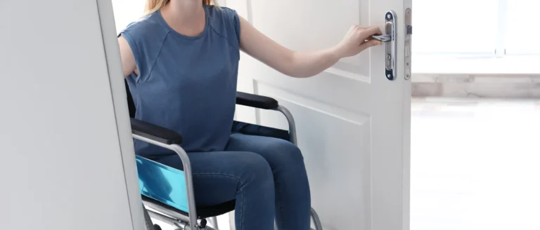 Eine Frau im Rollstuhl öffnet eine weiße Innentür.