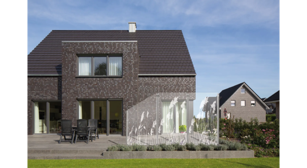 Glaszaun mit dekorativem Gräsermotiv vor der Terrasse eines modernen Wohnhauses.