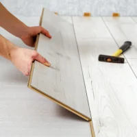 Zwei Hände verlegen hellen Holzlaminatboden mit Unterlage unter Vinylplatten auf dem Boden.